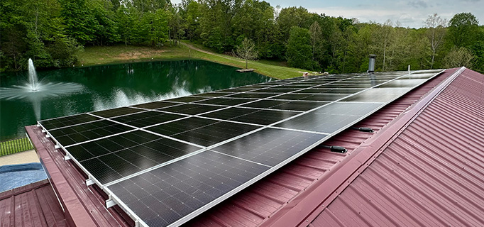 Solar panels on the roof of a building overlooking a pond.