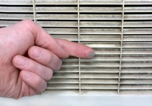 Finger showing thick dust buildup on a dirty air vent grille, highlighting the need for air duct cleaning services.