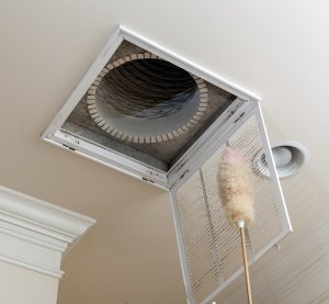 Ceiling air duct vent opened for cleaning with a duster, showing routine air duct cleaning in progress.