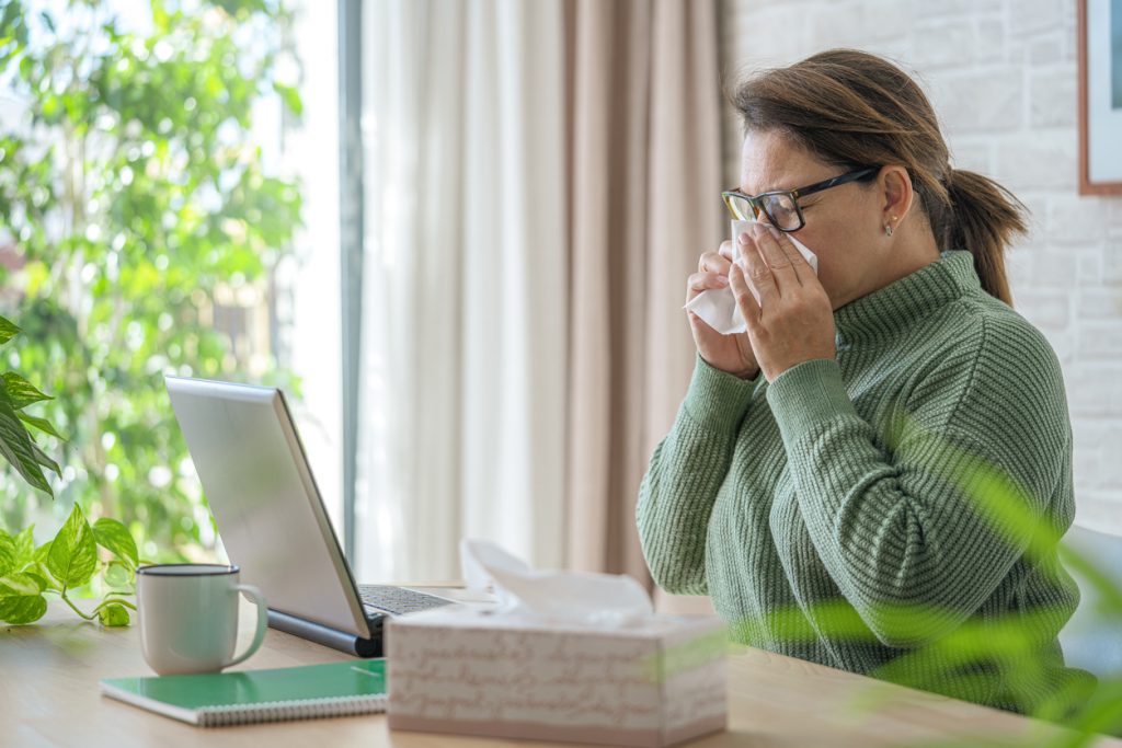Woman working on laptop blowing her nose with facial tissue